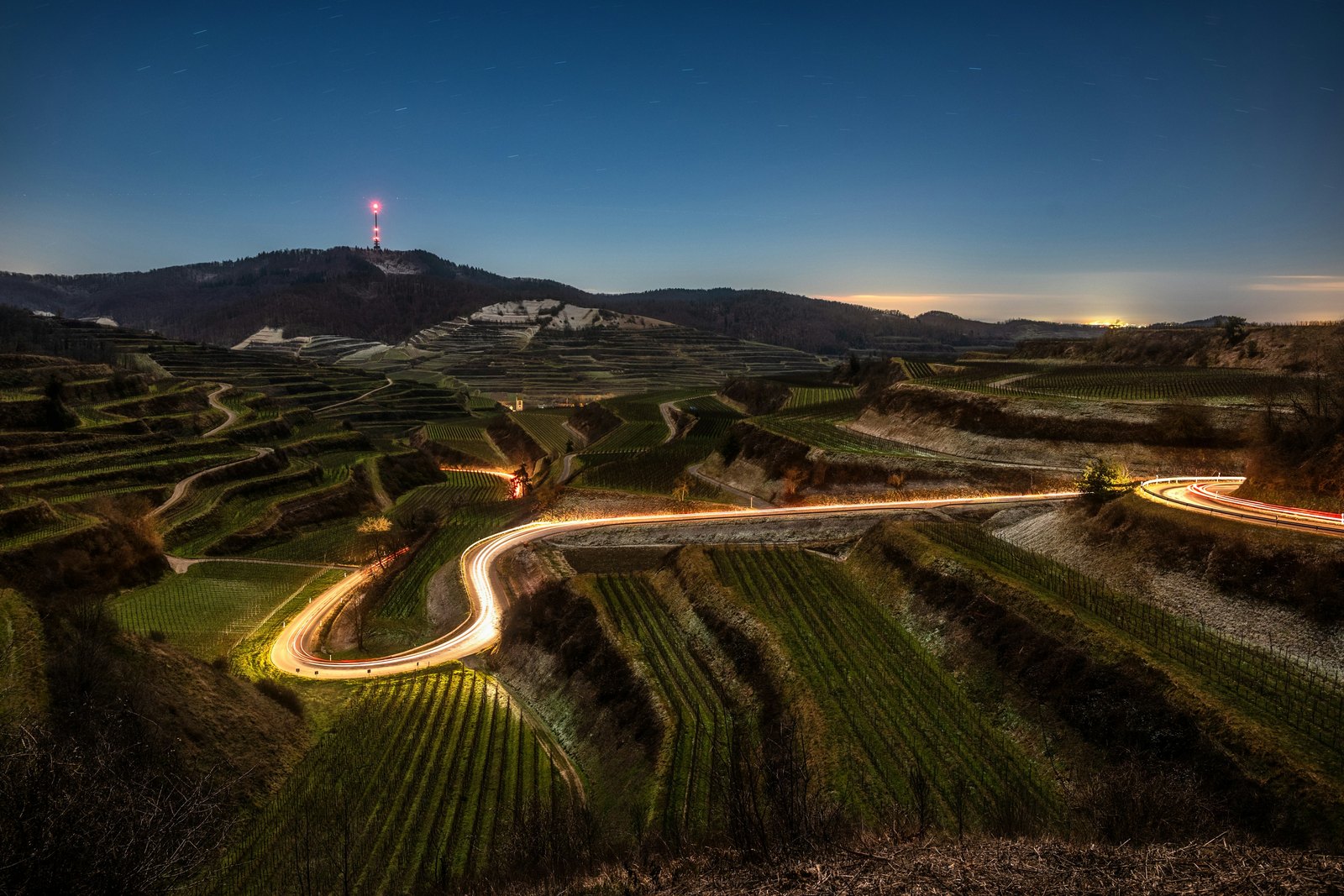 Serpentina mezi terasovitými vinicemi za modré hodiny, se světelnou stopou projíždějícího auta